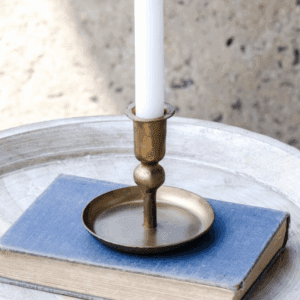 Brass candle holder with a white candle on a blue cloth.